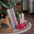 Load image into Gallery viewer, Rolls of colorful wrapping paper and ribbons with a Christmas tree in the background.
