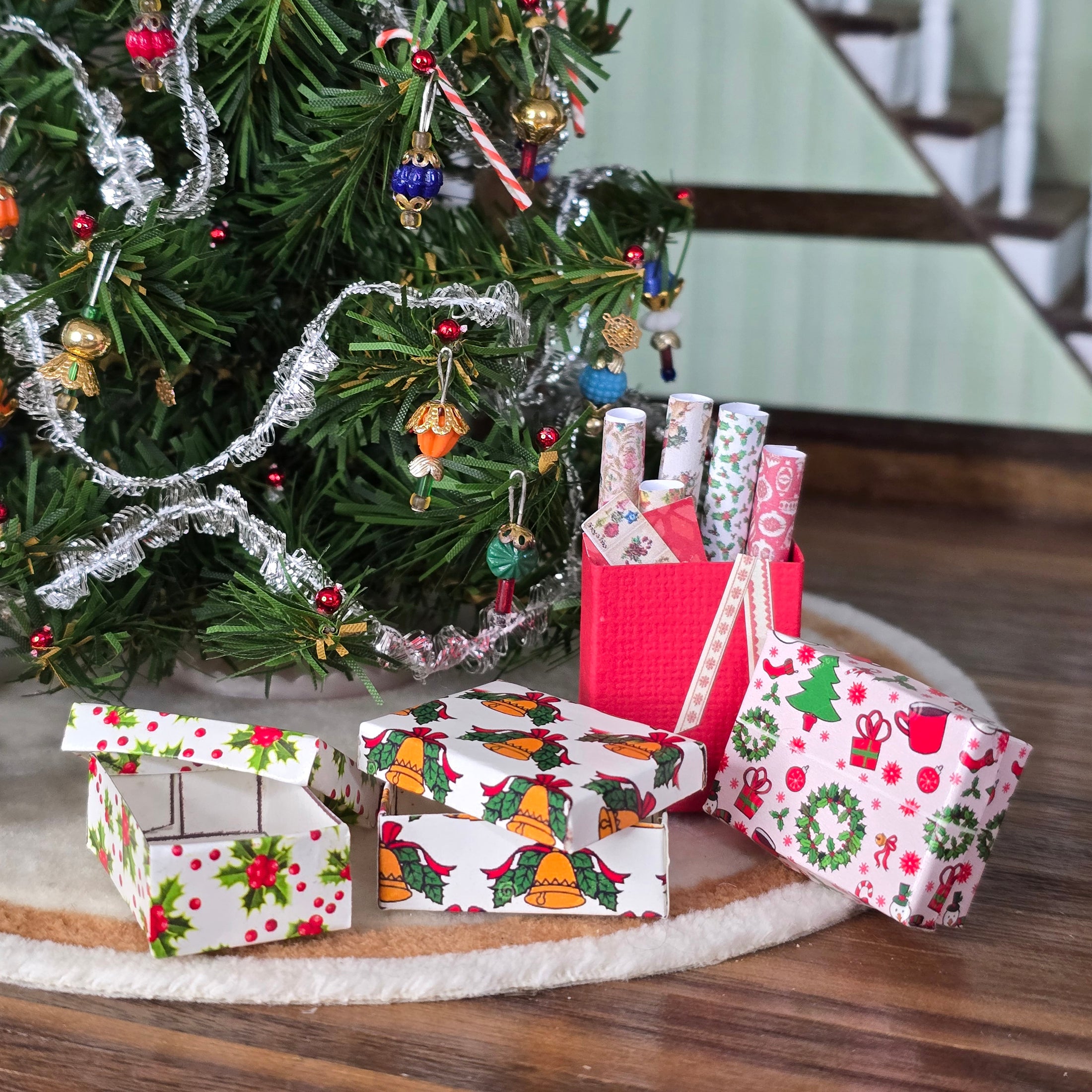 Christmas-themed Miniature dollhouse gift boxes and a tree with ornaments on a wooden surface.