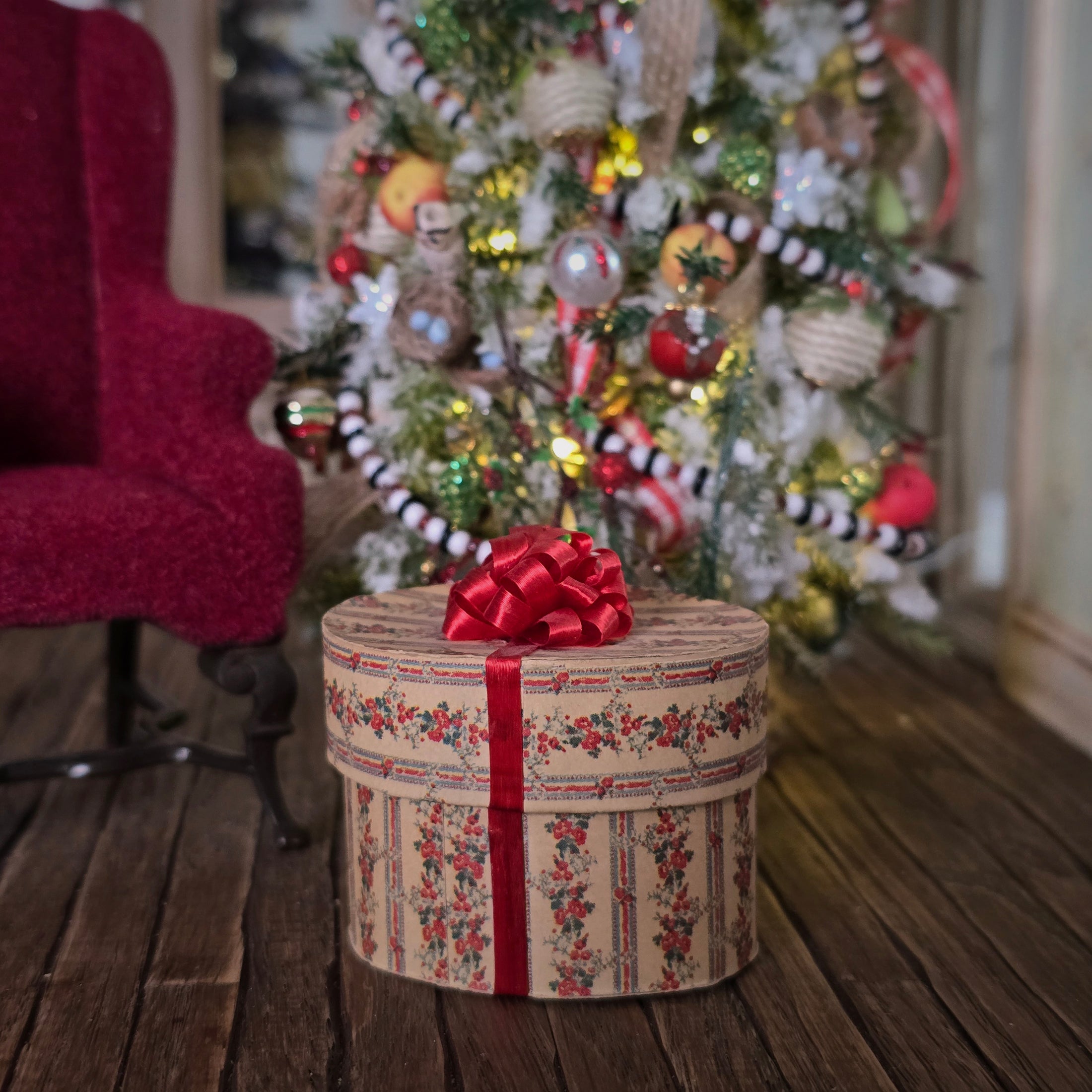 Decorative miniature dollhouse hat box with a red bow in front of a Christmas tree.