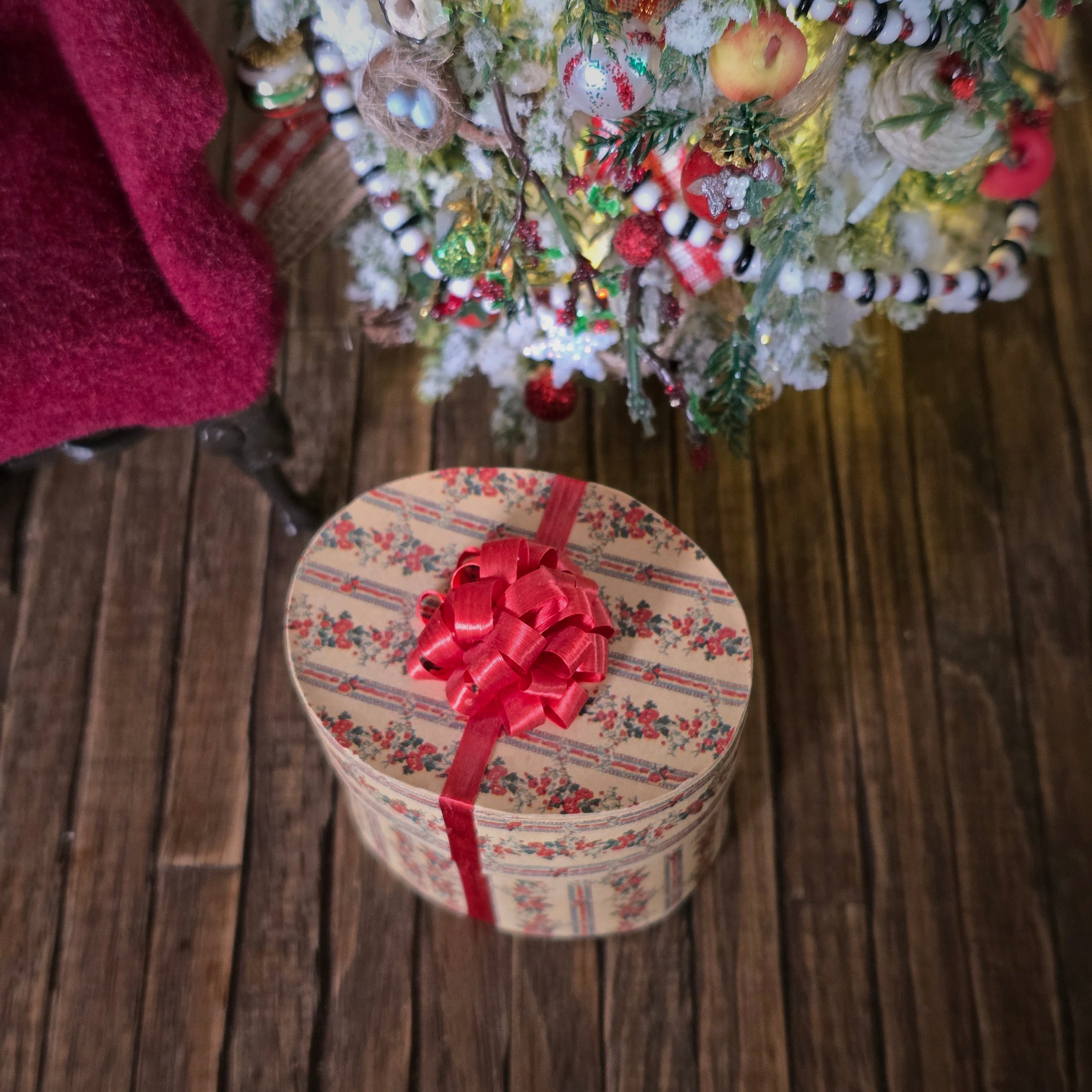 oval miniature dollhouse hat box with a red ribbon, and a Christmas tree in the background