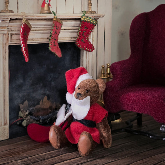 Dollhouse Teddy bear in a Santa outfit sitting in front of a fireplace with stockings.