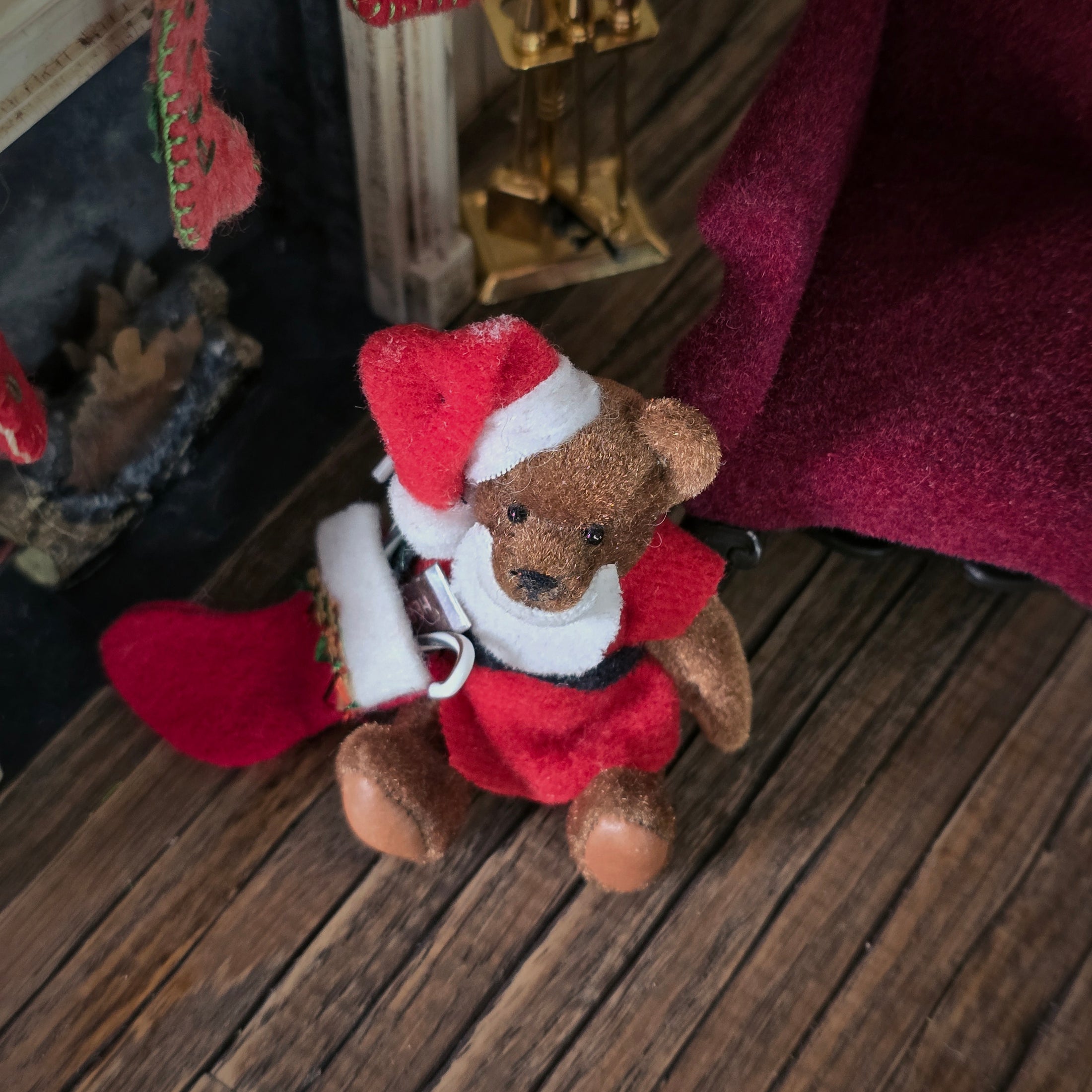 Dollhouse Small teddy bear in a Santa outfit sitting on a wooden floor with Christmas stockings in the background.