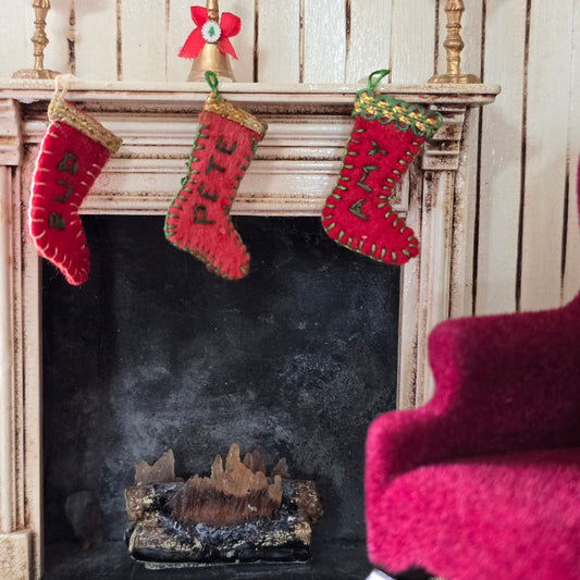 Three red Christmas stockings hanging above a fireplace with a velvet chair in the foreground.