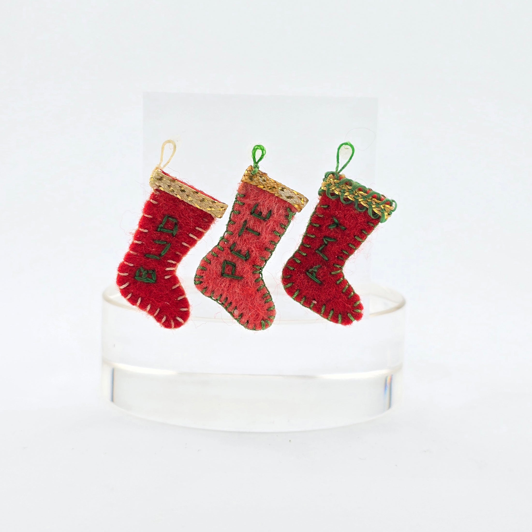Three red Christmas stockings with gold trim on a white pedestal against a white background