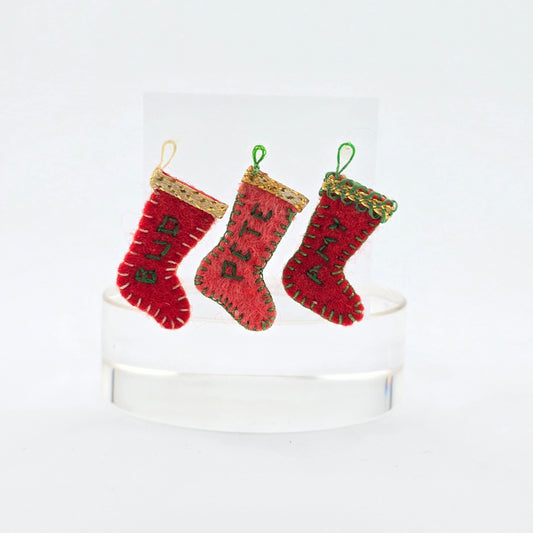Three red Christmas stockings with gold trim on a white pedestal against a white background