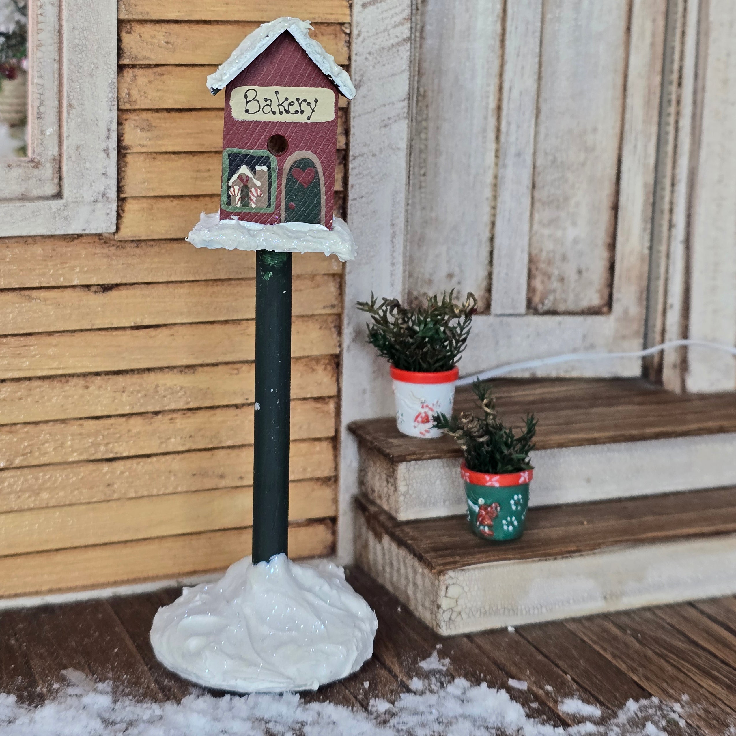 miniature dollhouse Christmas bakery birdhouse and potted plant set in front of yellow country house
