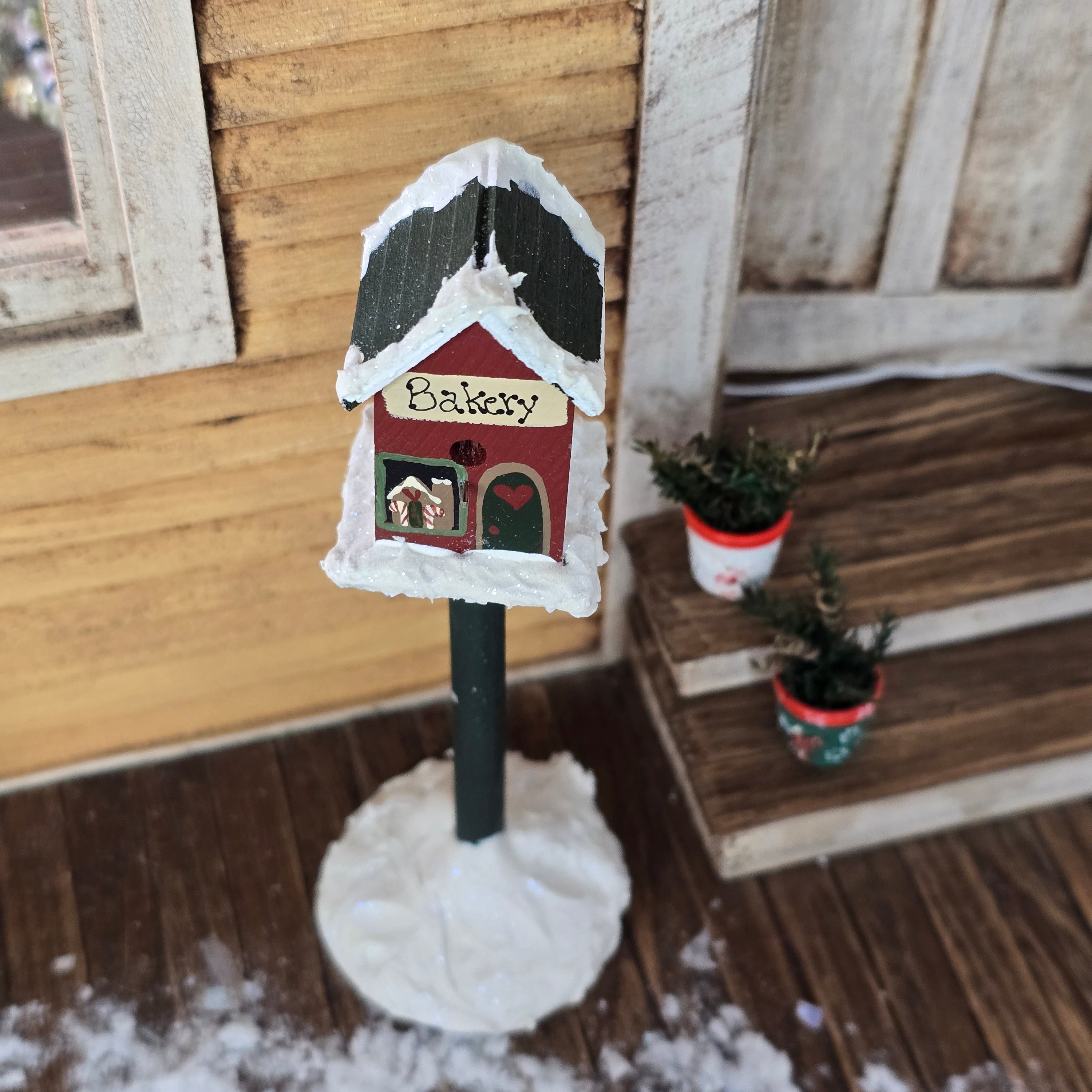 top view of miniature dollhouse Christmas bakery birdhouse and potted plant set in front of yellow country house
