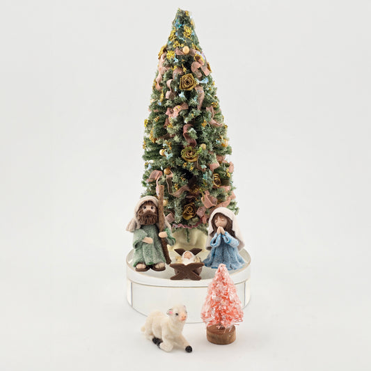 Decorative Christmas scene with a tree, nativity figures, and a small pink tree on a white background.