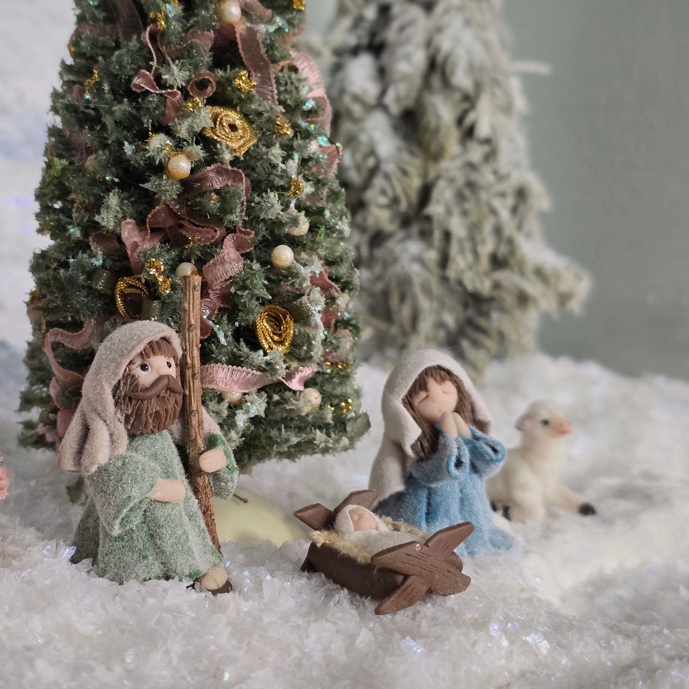miniature dollhouse Nativity scene with figures of Mary, Joseph, and baby Jesus in a manger, set against a decorated Christmas tree.