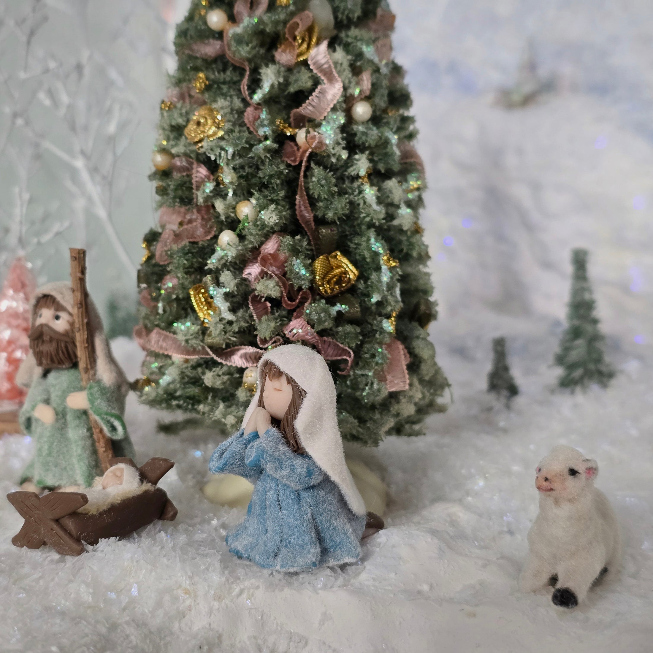 miniature dollhouse Nativity scene with figures and a decorated Christmas tree in a snowy setting