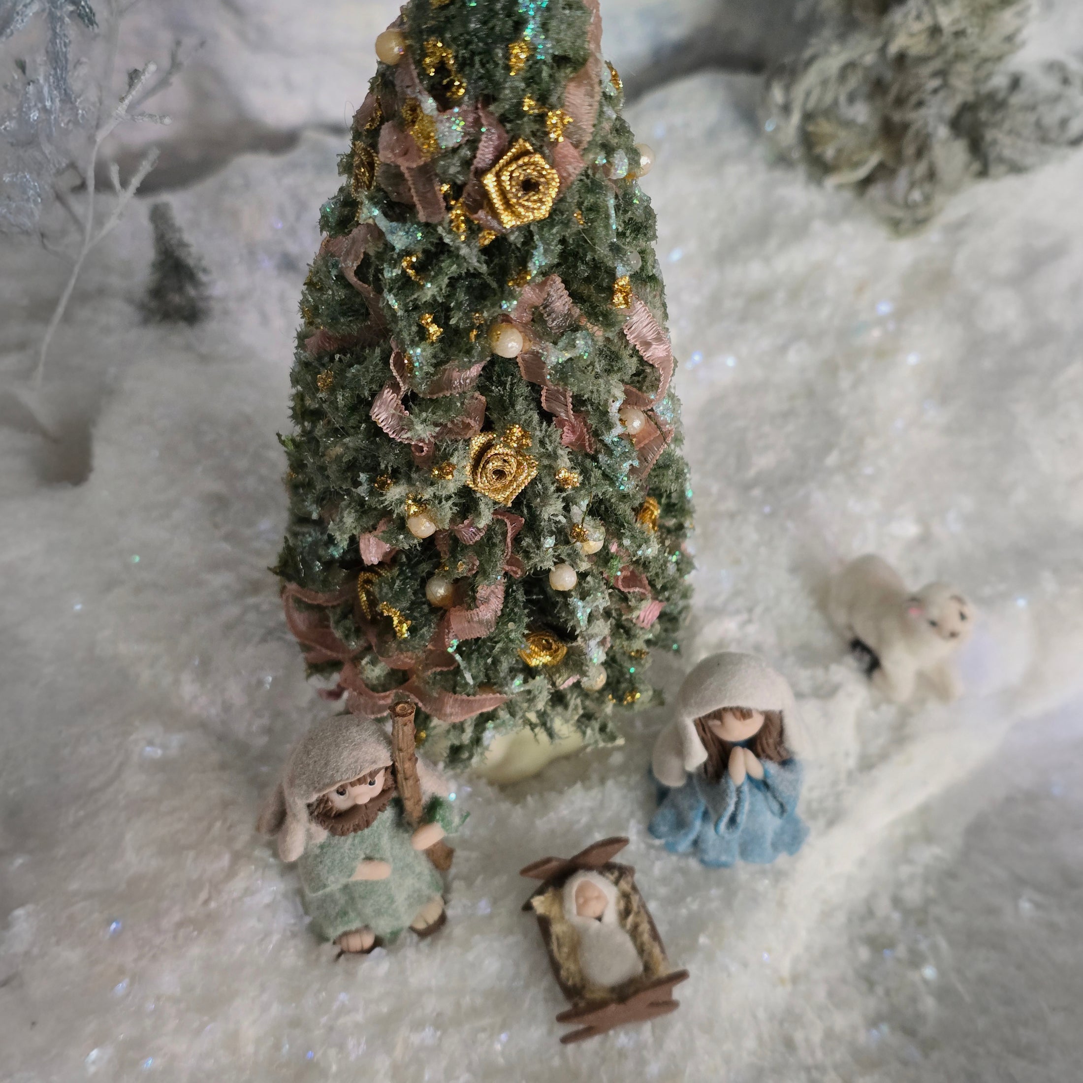miniature dollhouse Christmas tree with ornaments and small figures on a snowy background