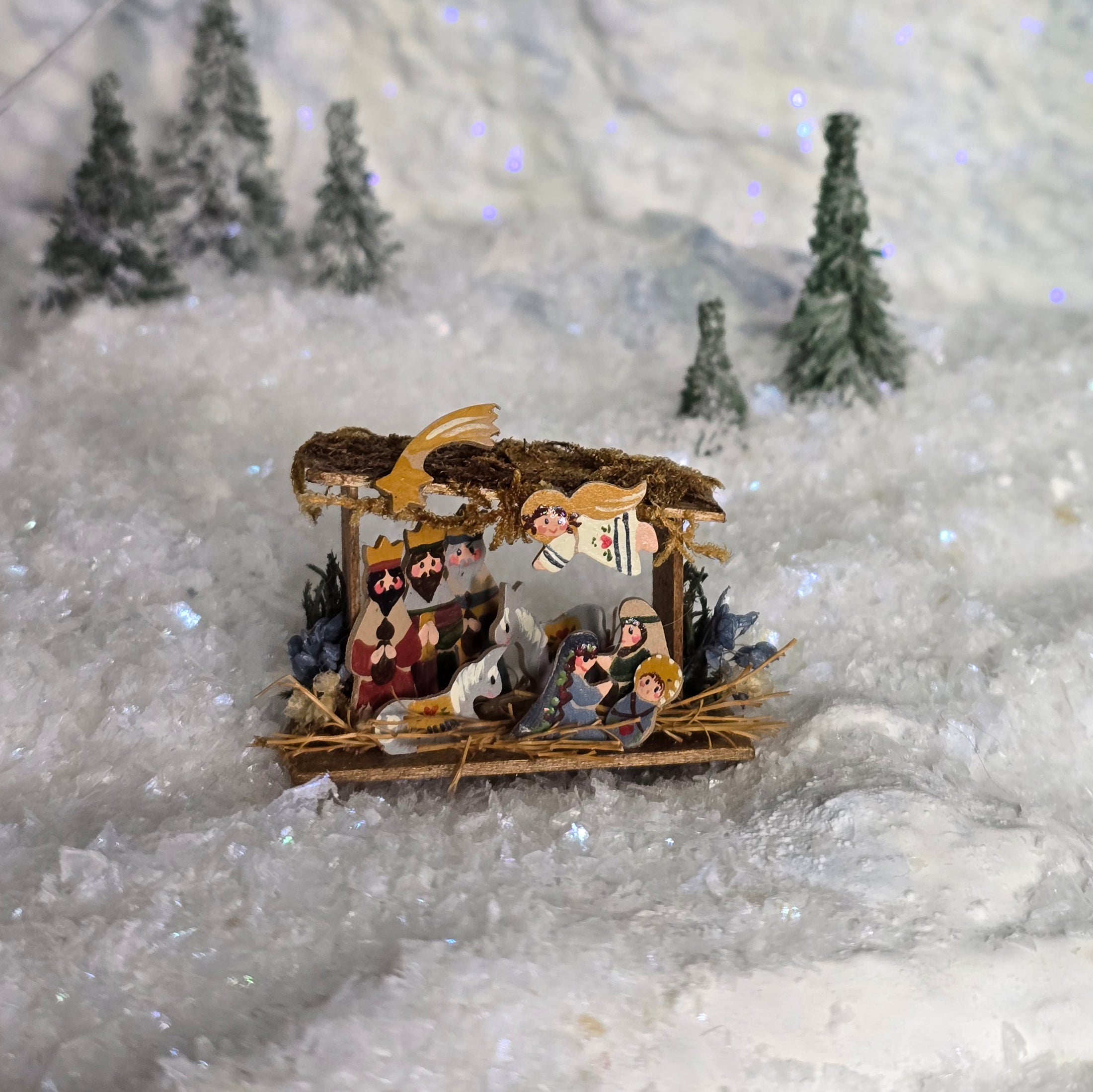 Miniature nativity scene set against a snowy landscape with trees.