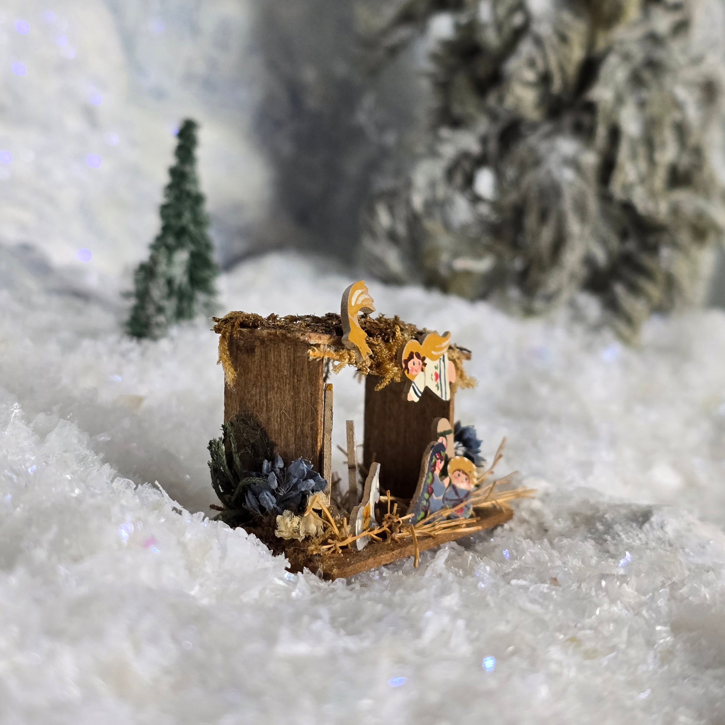 Miniature nativity scene in a snowy landscape with trees in the background
