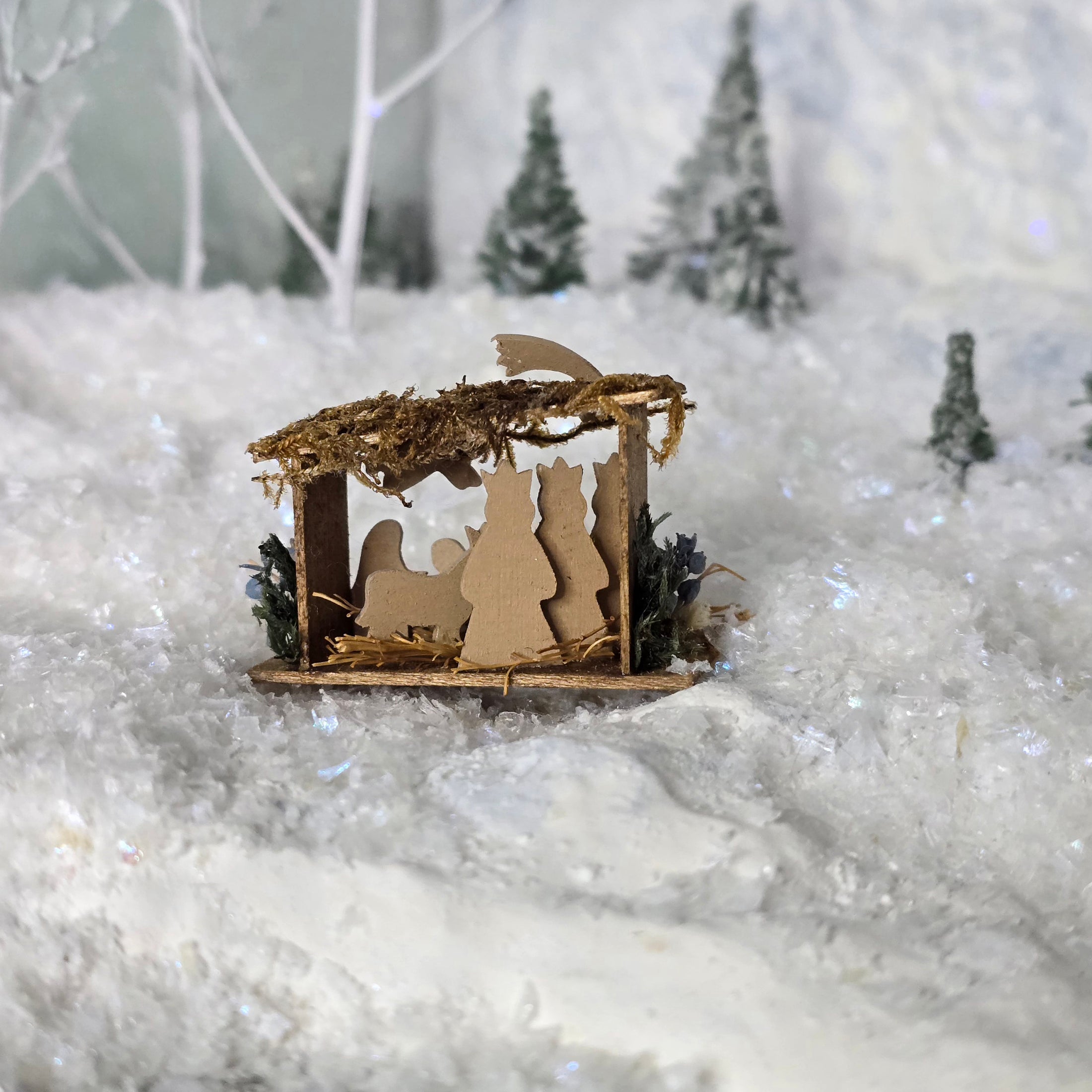 Miniature nativity scene (back view) on a snowy background.