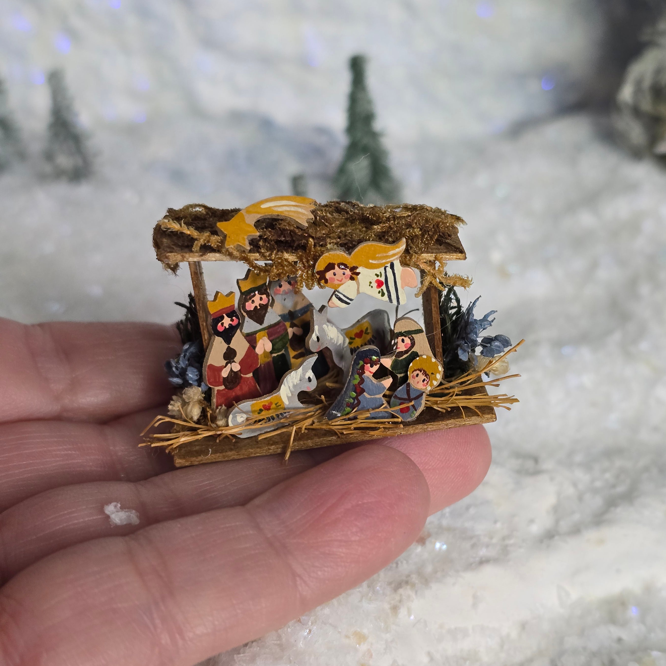 Miniature nativity scene held in a hand with a blurred snowy background