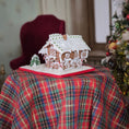 Load image into Gallery viewer, Gingerbread house on a plaid tablecloth with a Christmas tree in the background
