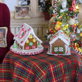 Load image into Gallery viewer, Two decorated gingerbread houses on a table with a Christmas tree in the background.
