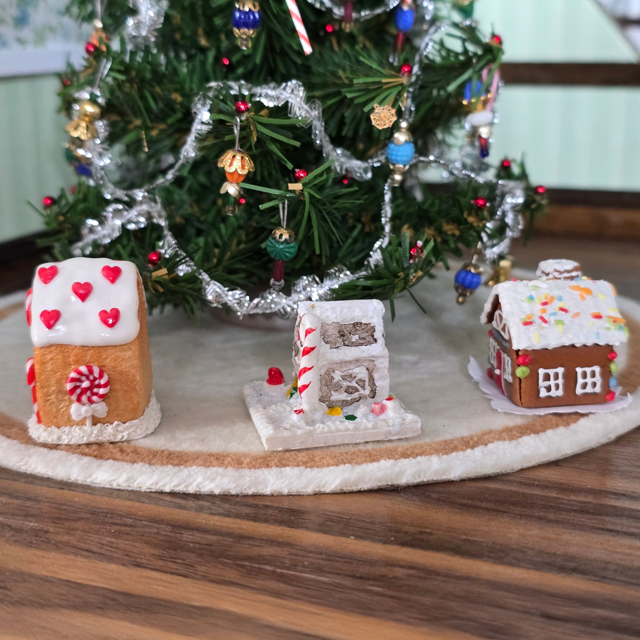 Three miniature gingerbread houses  with a decorated Christmas tree in the background.