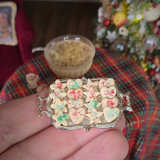 Miniature cookies on a silver tray held by a hand with a Christmas-themed background