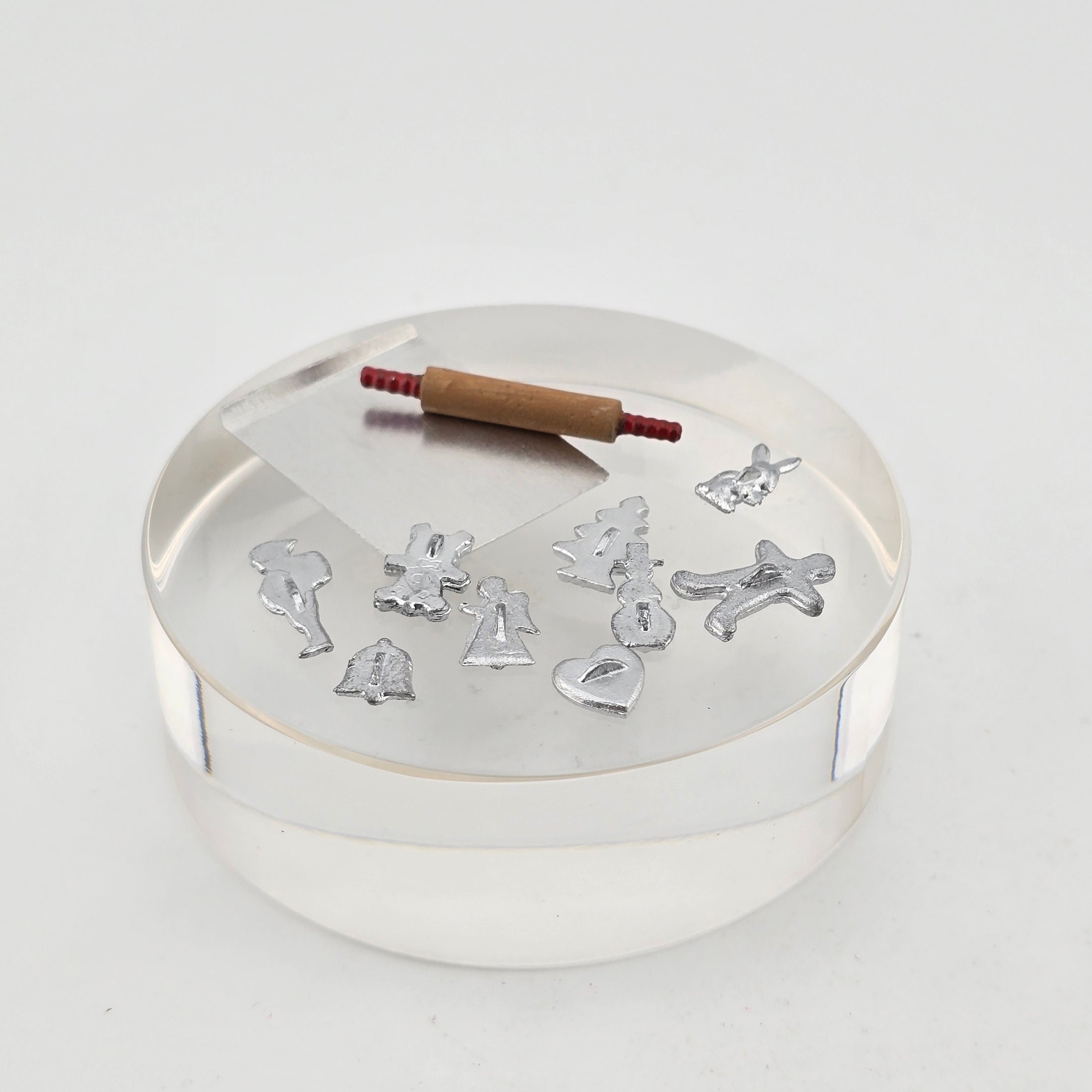 Miniature dollhouse metal Christmas cookie cutters with a rolling pin and a metal baking sheet, all on a white surface