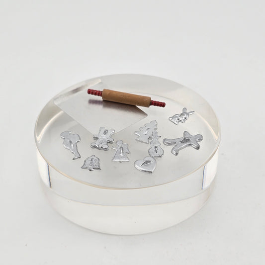 Miniature dollhouse metal Christmas cookie cutters with a rolling pin and a metal baking sheet, all on a white surface