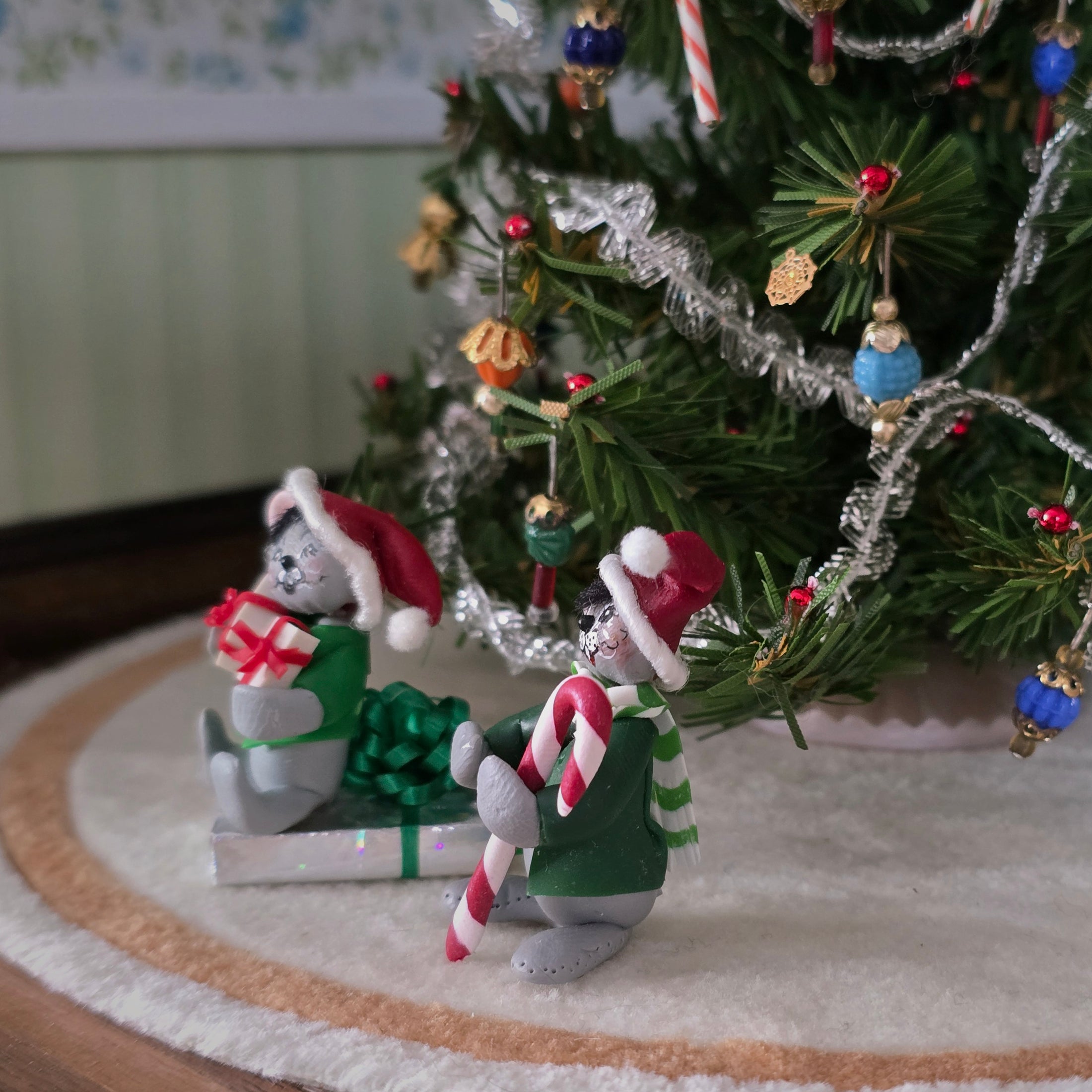 Two Christmas-themed Annalee style mice figurines in front of a decorated tree.