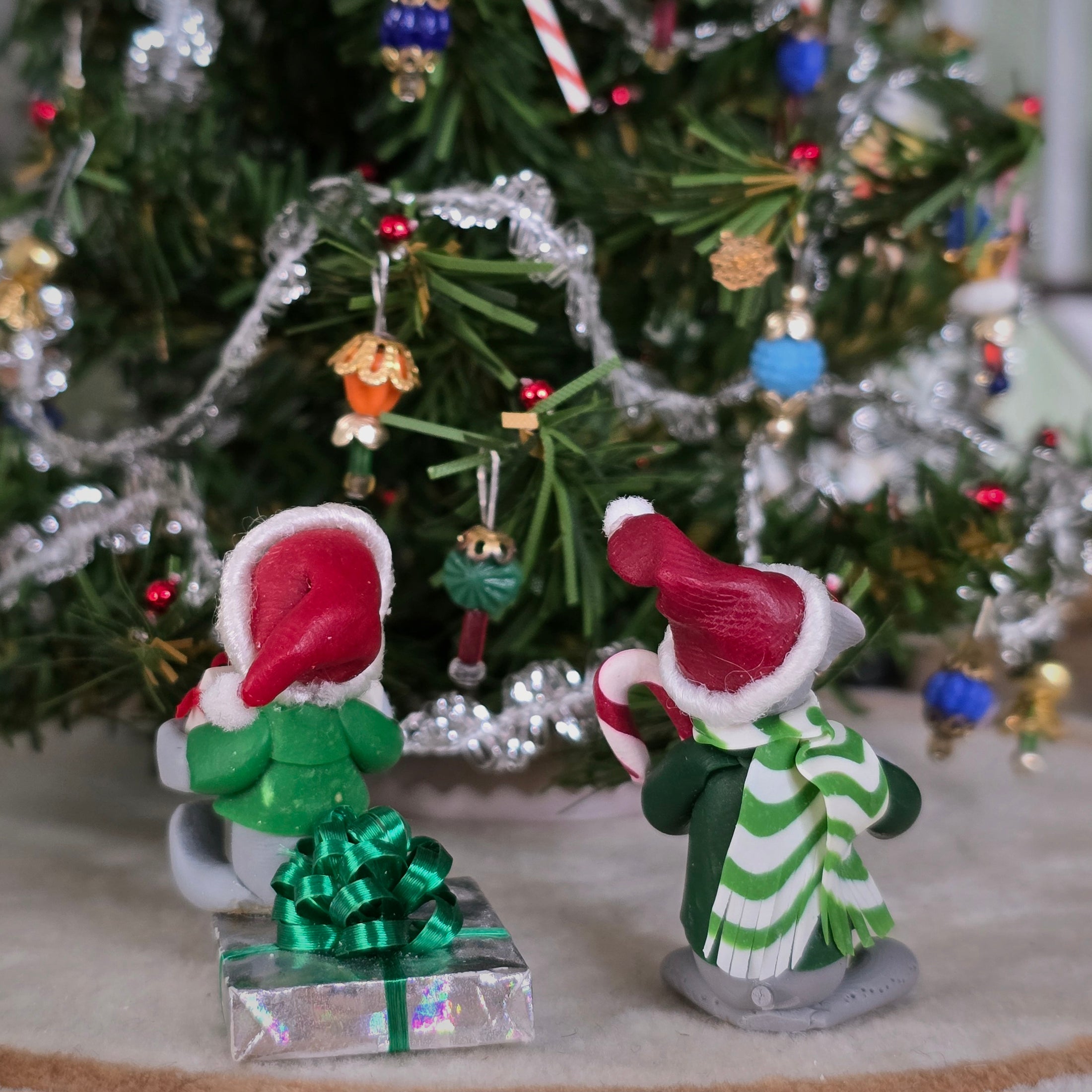 Two Christmas-themed Annalee style mice figurines in front of a decorated tree. (back view)