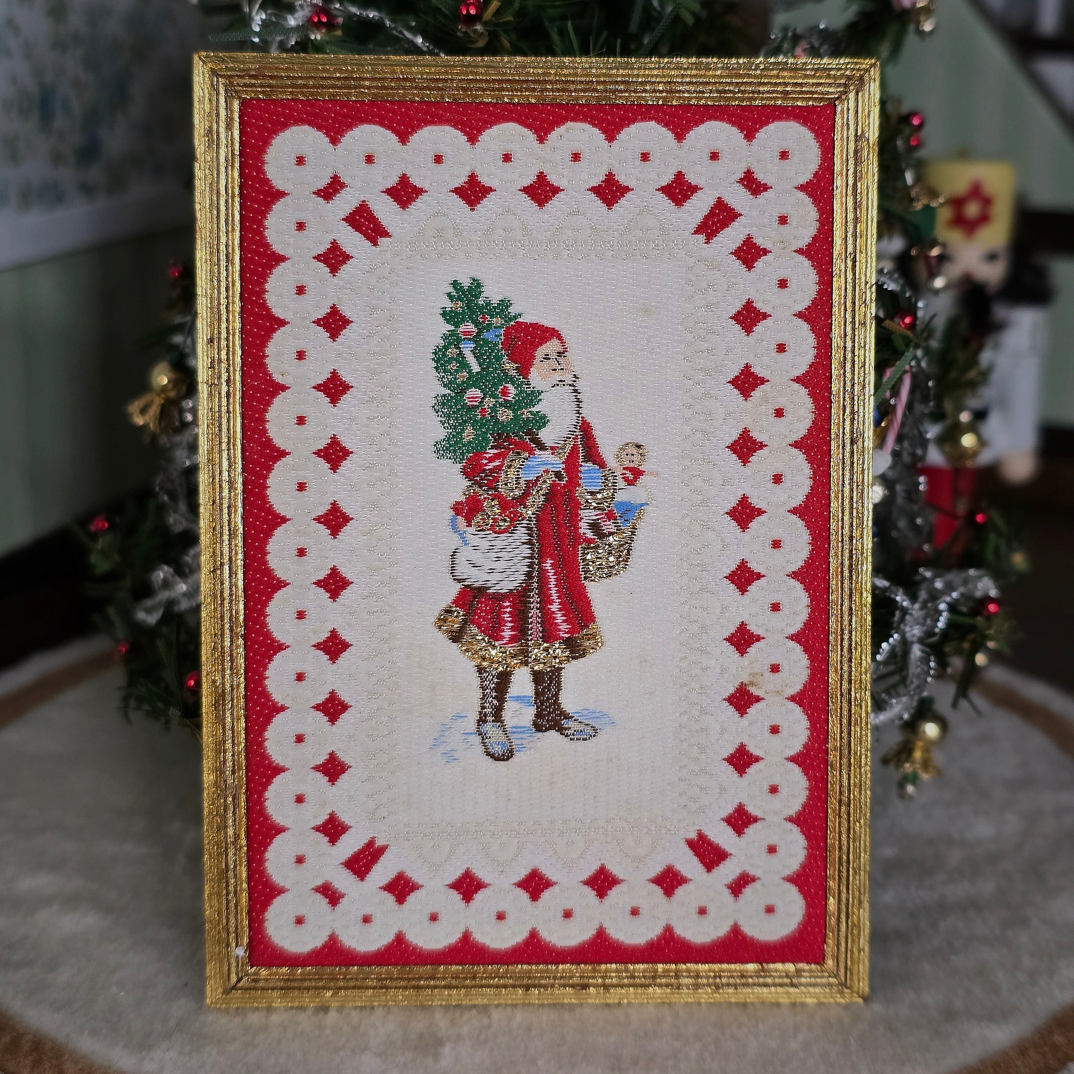 Framed miniature embroidered Victorian Santa Claus leaning against a Christmas tree.