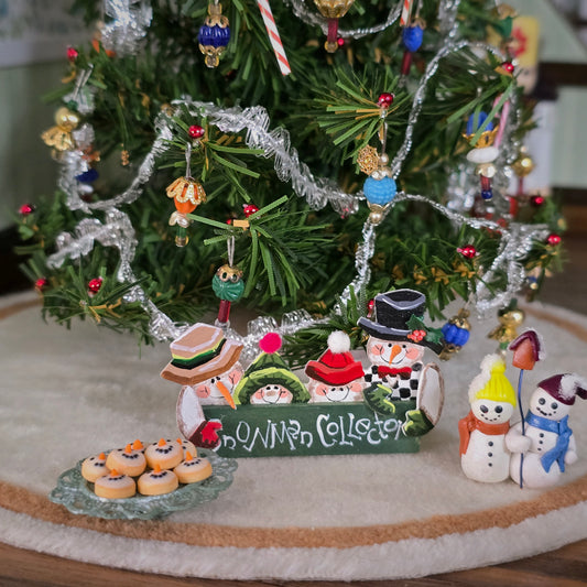 miniature dollhouse snowmen-themed sign, shelf sitter and cookie platter under christmas tree