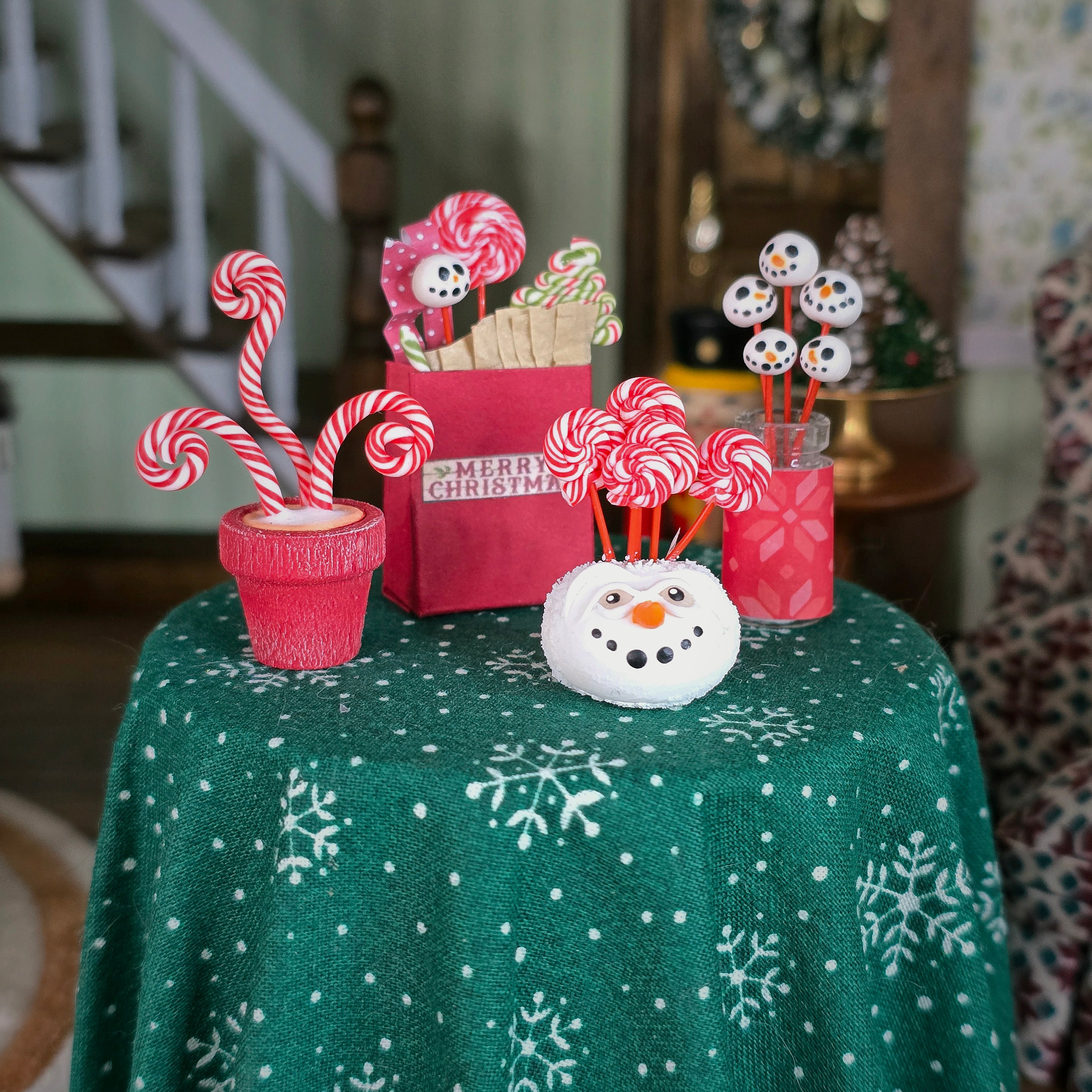 Decorative Christmas items on a table with a green tablecloth featuring snowflake patterns.