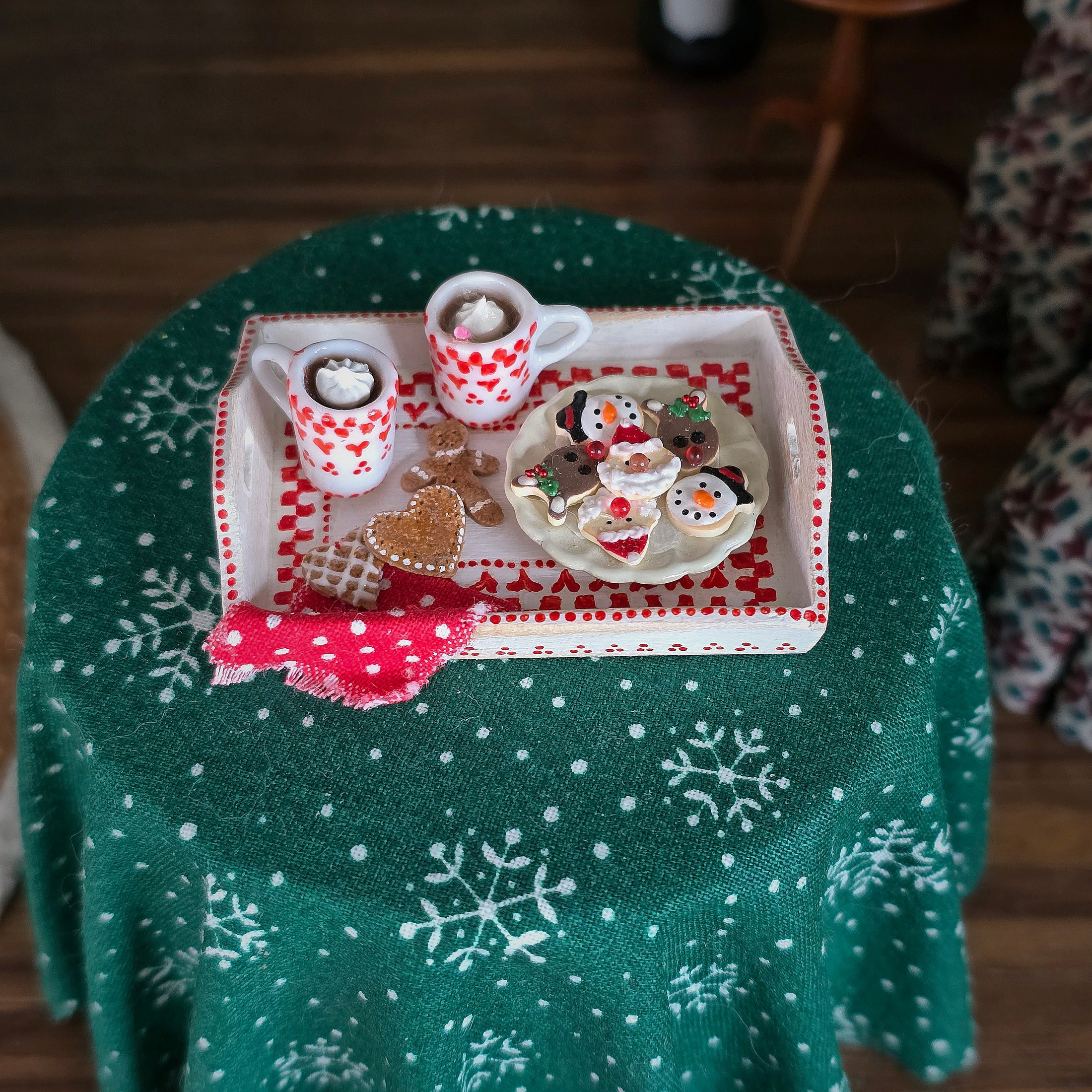 Decorative tray with cookies and mugs on a green tablecloth with snowflake pattern