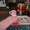 Load image into Gallery viewer, Miniature red and white checkered cup with a straw held by a hand, blurred Christmas scene in the background.
