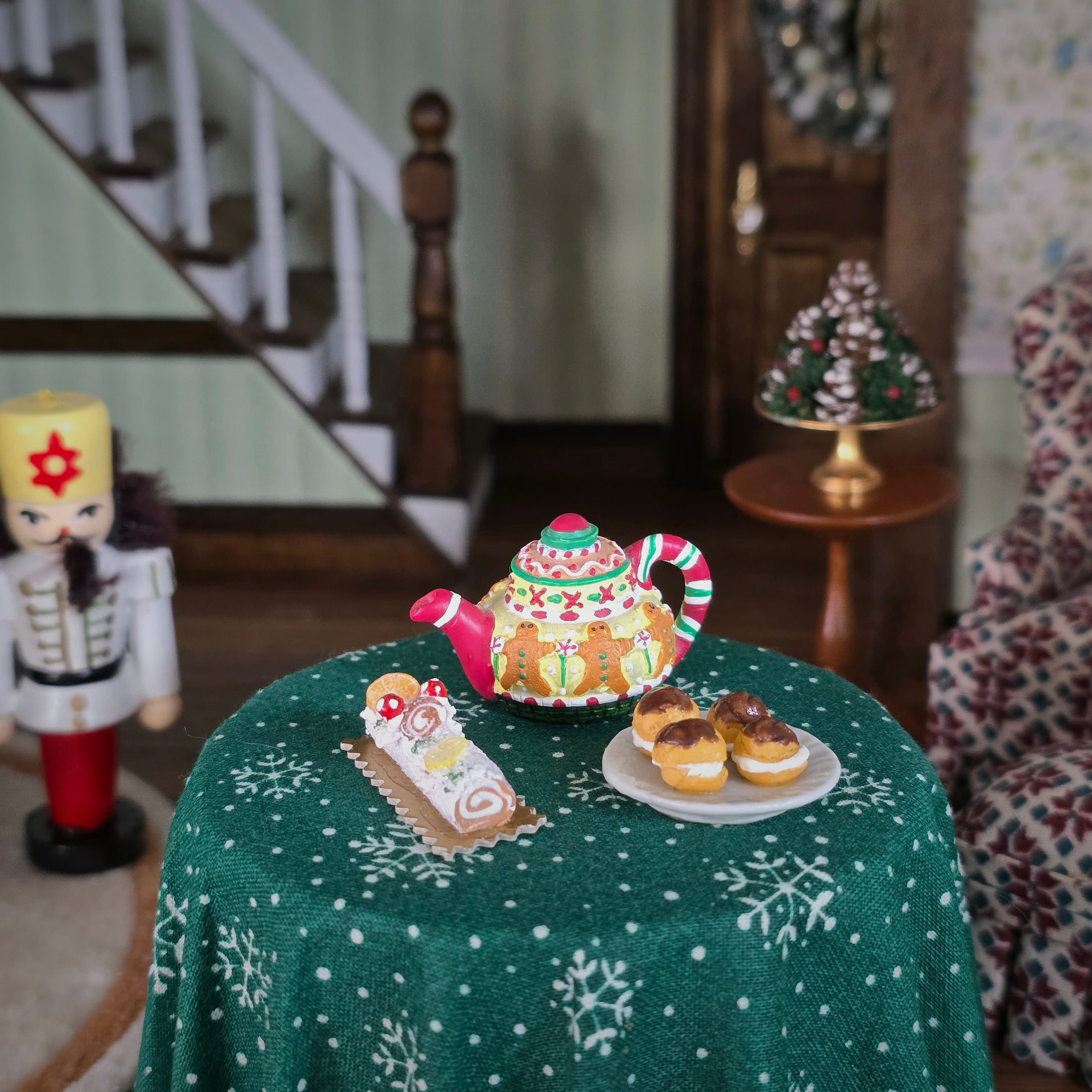 Decorative teapot on a table with a green tablecloth, surrounded by Christmas-themed items.