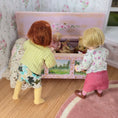 Load image into Gallery viewer, Two Catherine Muniere Dolls interacting with a toy box in a room with floral wallpaper.
