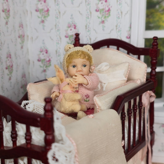 Catherine Muniere doll with a rabbit sitting on a wooden crib with floral wallpaper in the background.