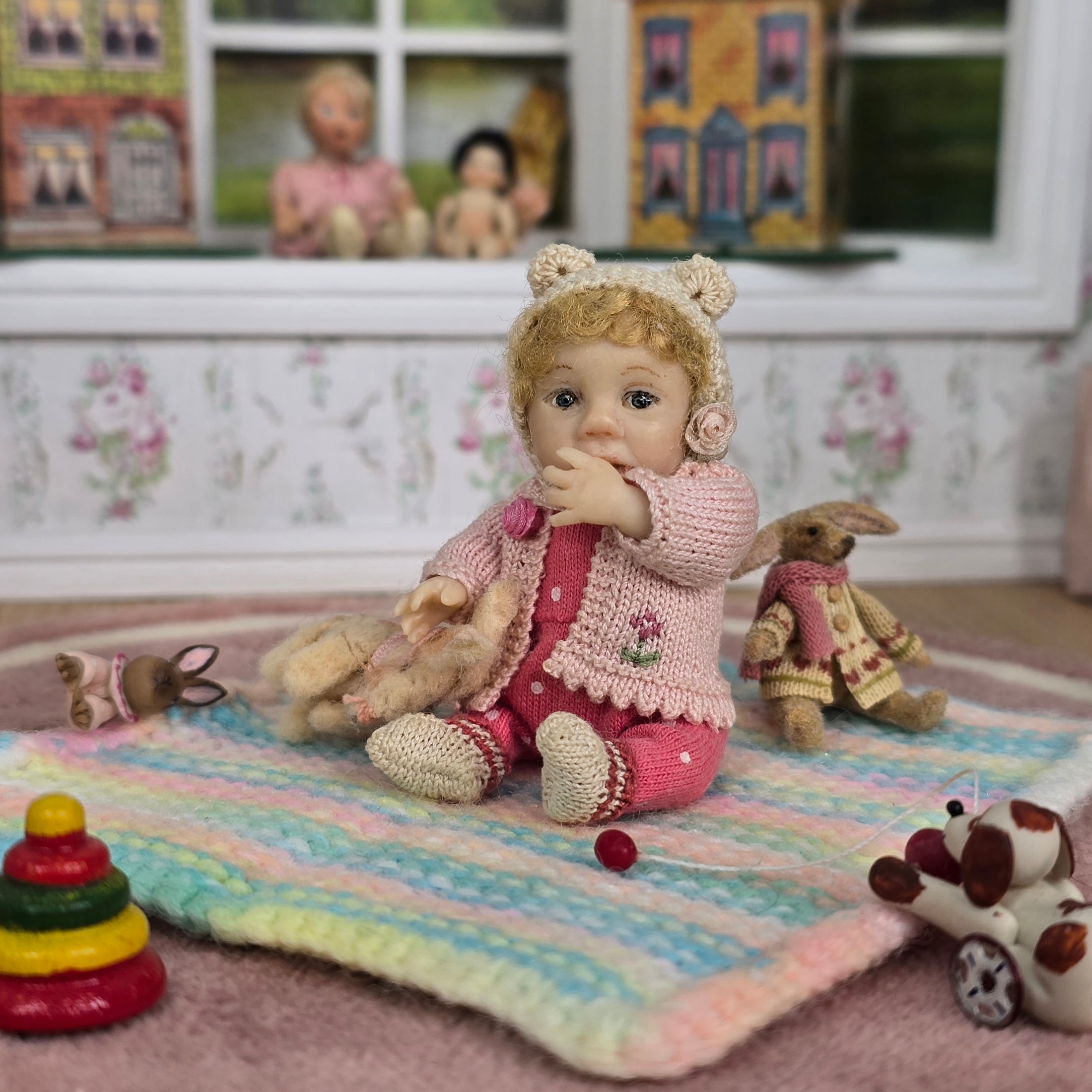 Catherine Muniere doll in a pink outfit sitting on a colorful blanket with toys around