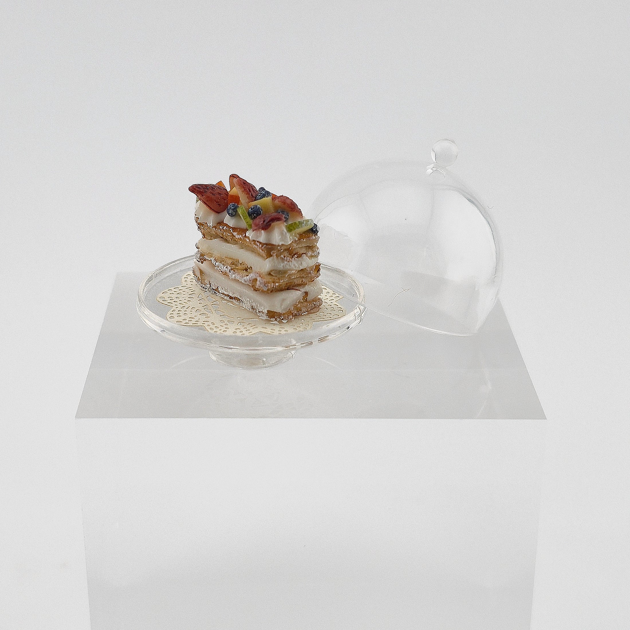 Shay Aaron Layered pastry with fruit on a small stand against a white background