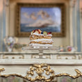 Load image into Gallery viewer, Delicate layered pastry miniature on a cake stand with a blurred classical painting in the background

