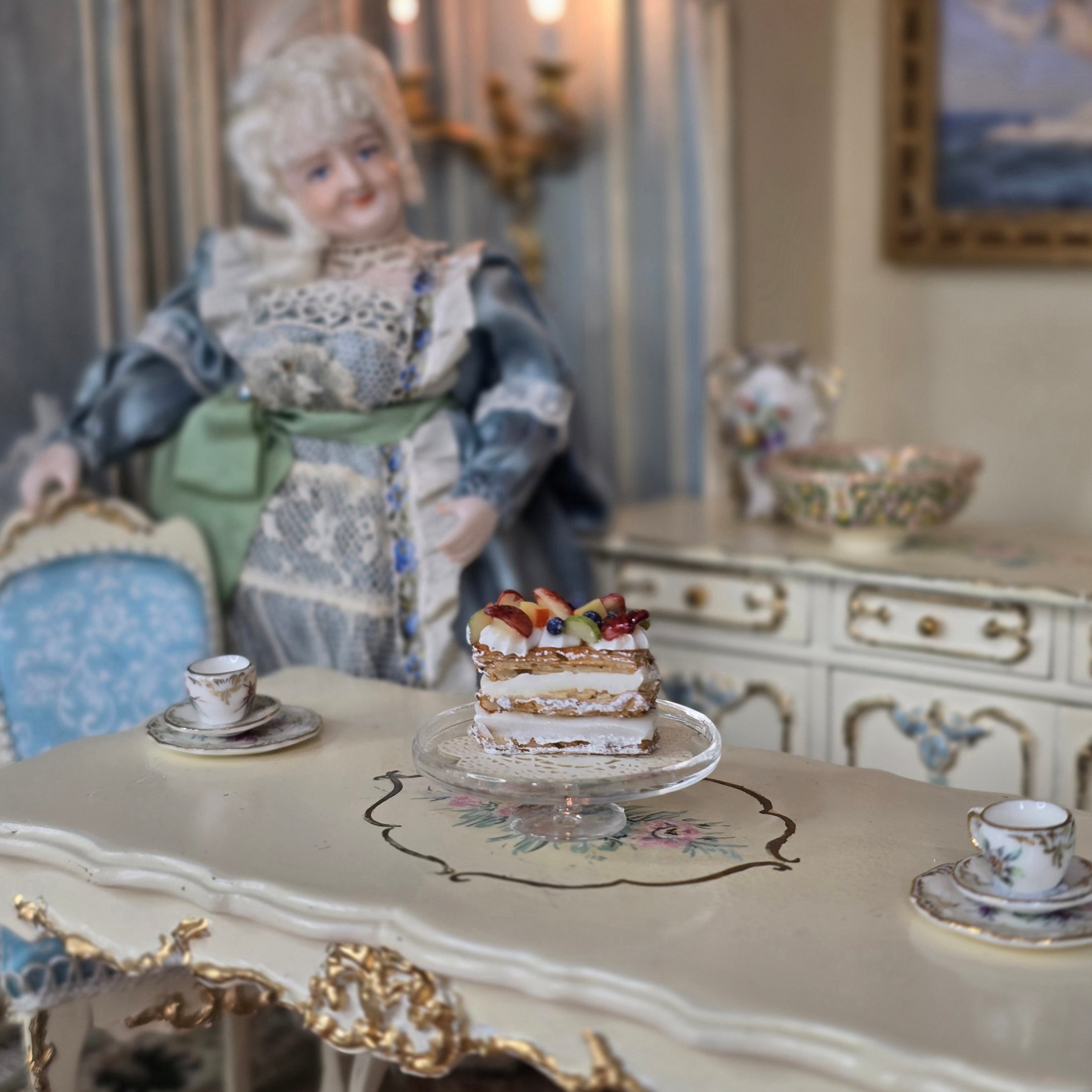 Miniature doll in a decorative setting with a pastry on a table
