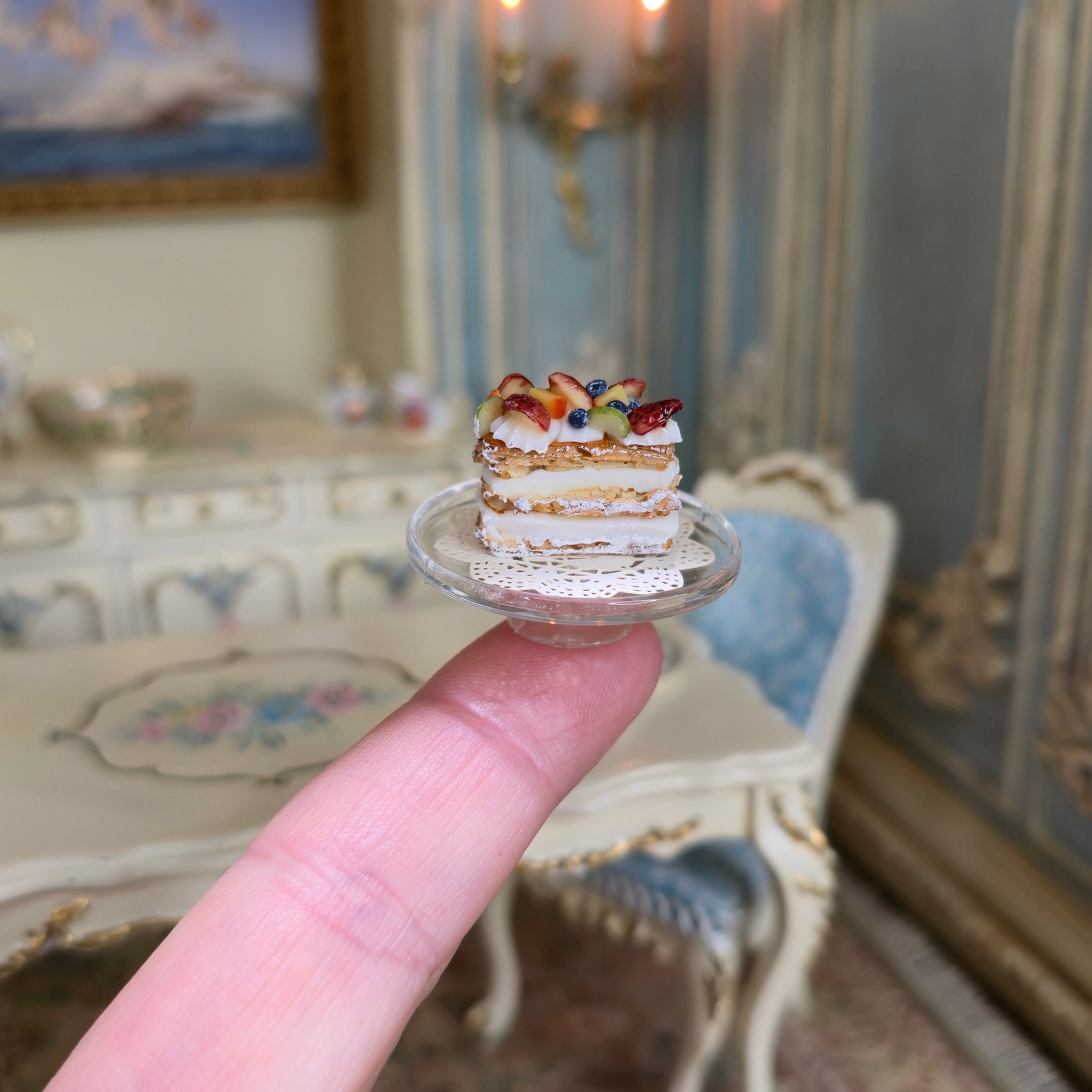Miniature pastry held on a finger with ornate furniture in the background
