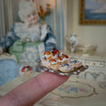 Load image into Gallery viewer, Miniature dessert on a silver plate held by a finger, with a doll in the background
