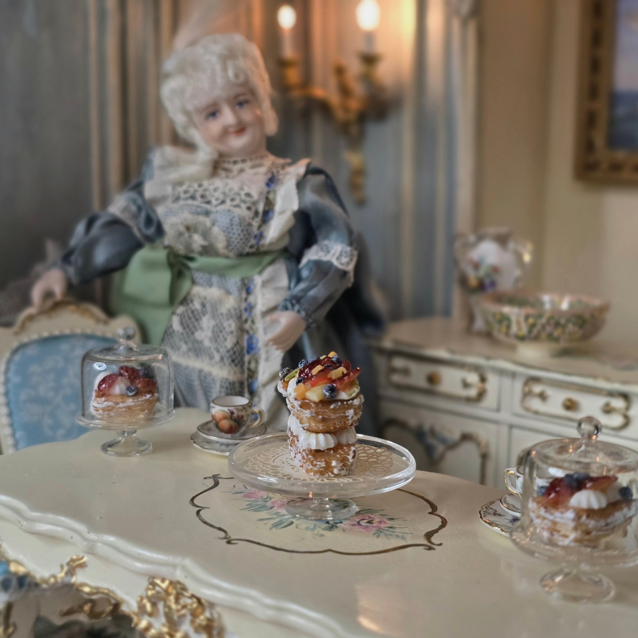 Vintage doll in a decorative setting with a table of pastries and tea cups.