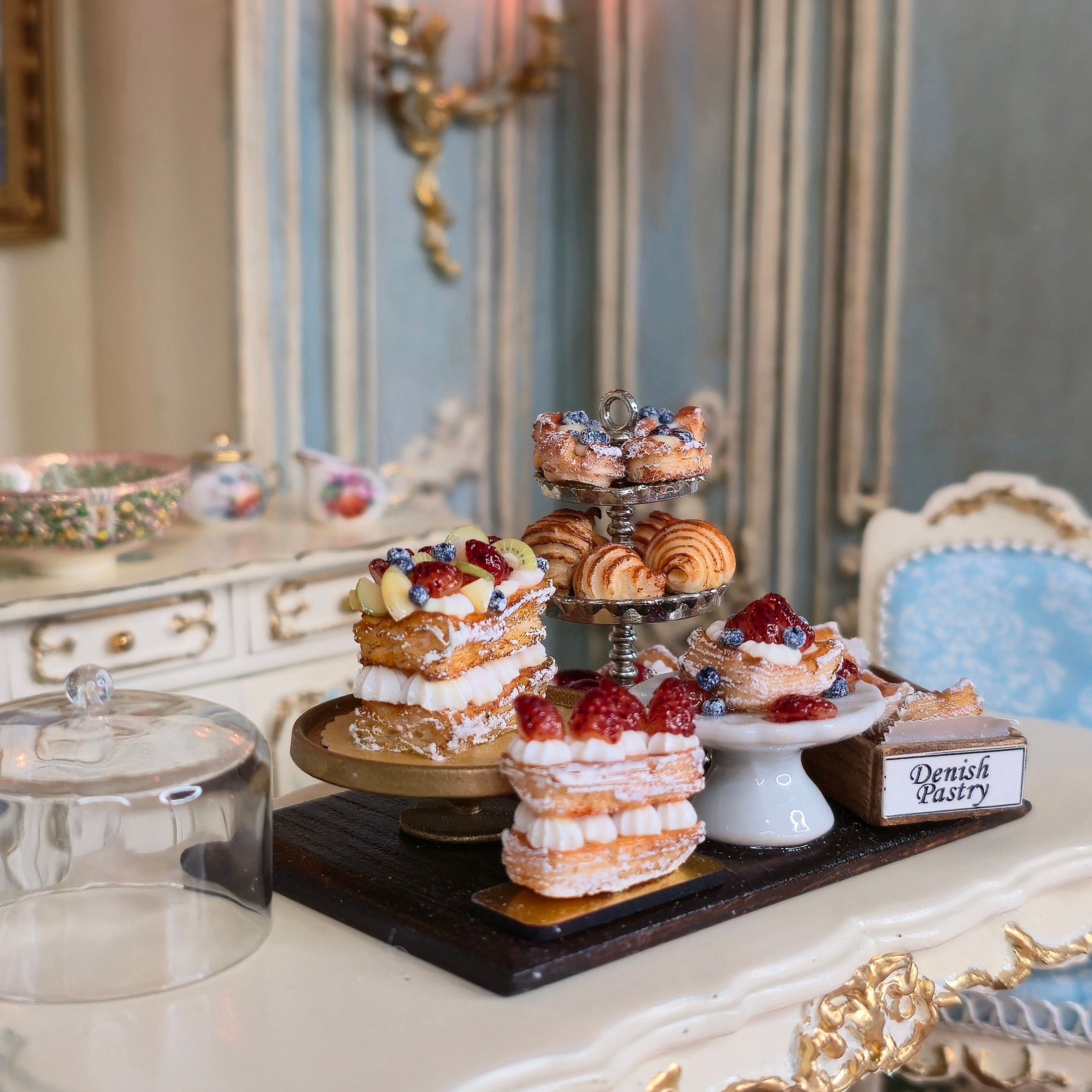 Three-tiered dessert stand with pastries on a decorative table.