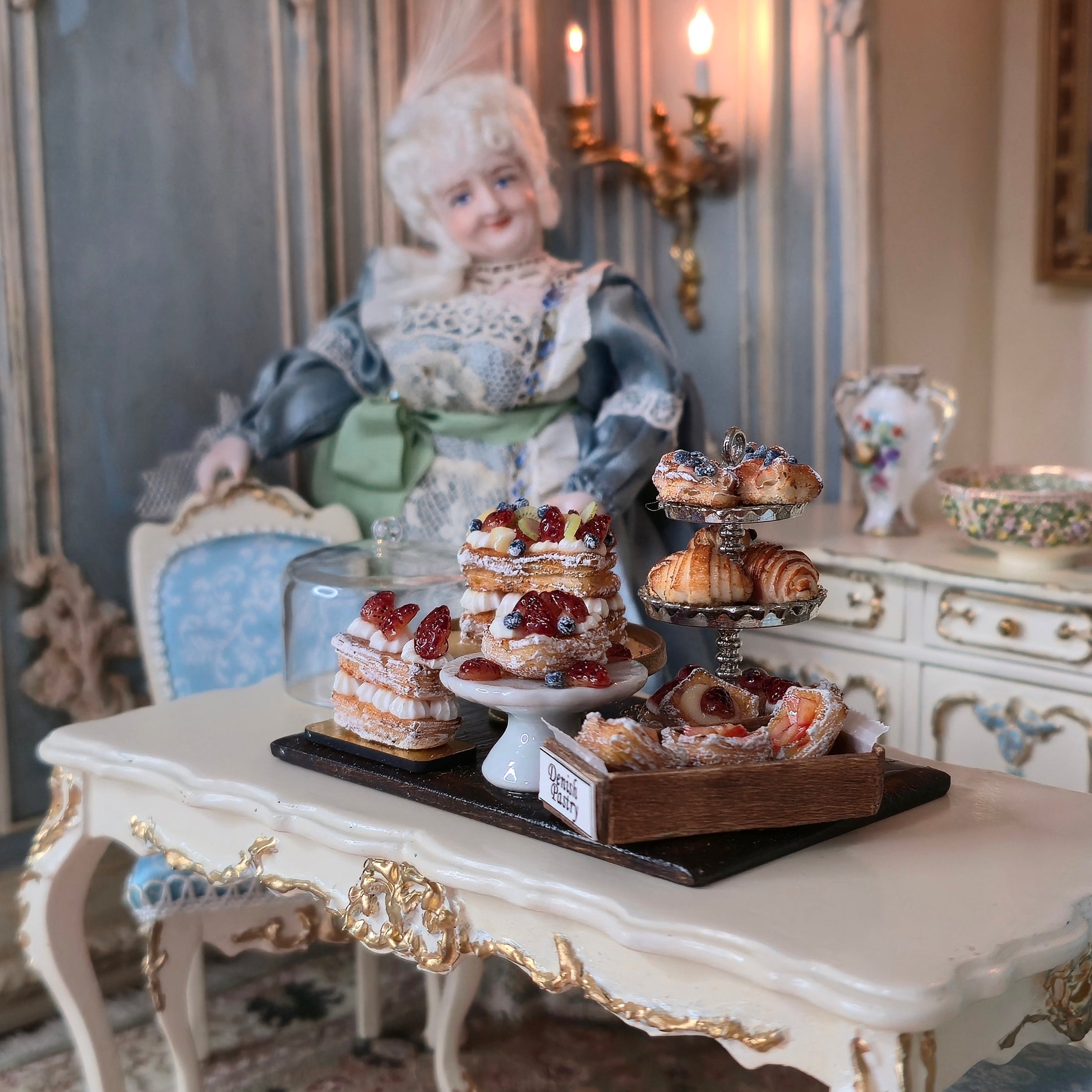 Miniature doll with a table of pastries in a decorative setting
