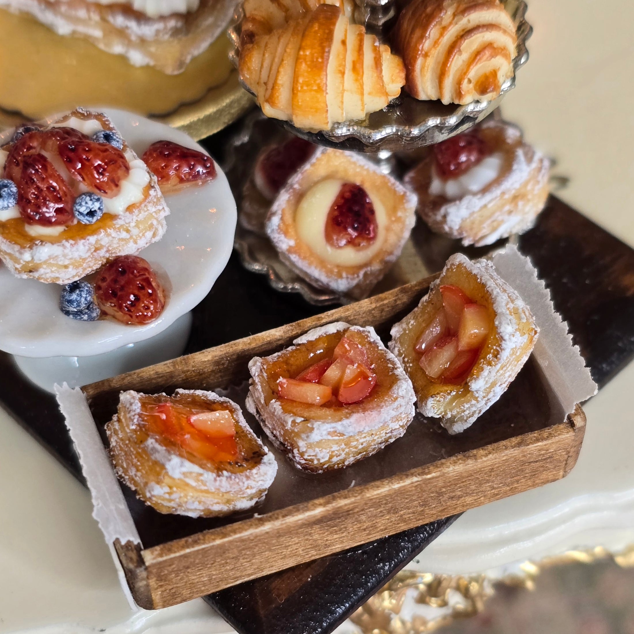 Assorted miniature pastries including strawberry tarts and croissants on a tiered stand.
