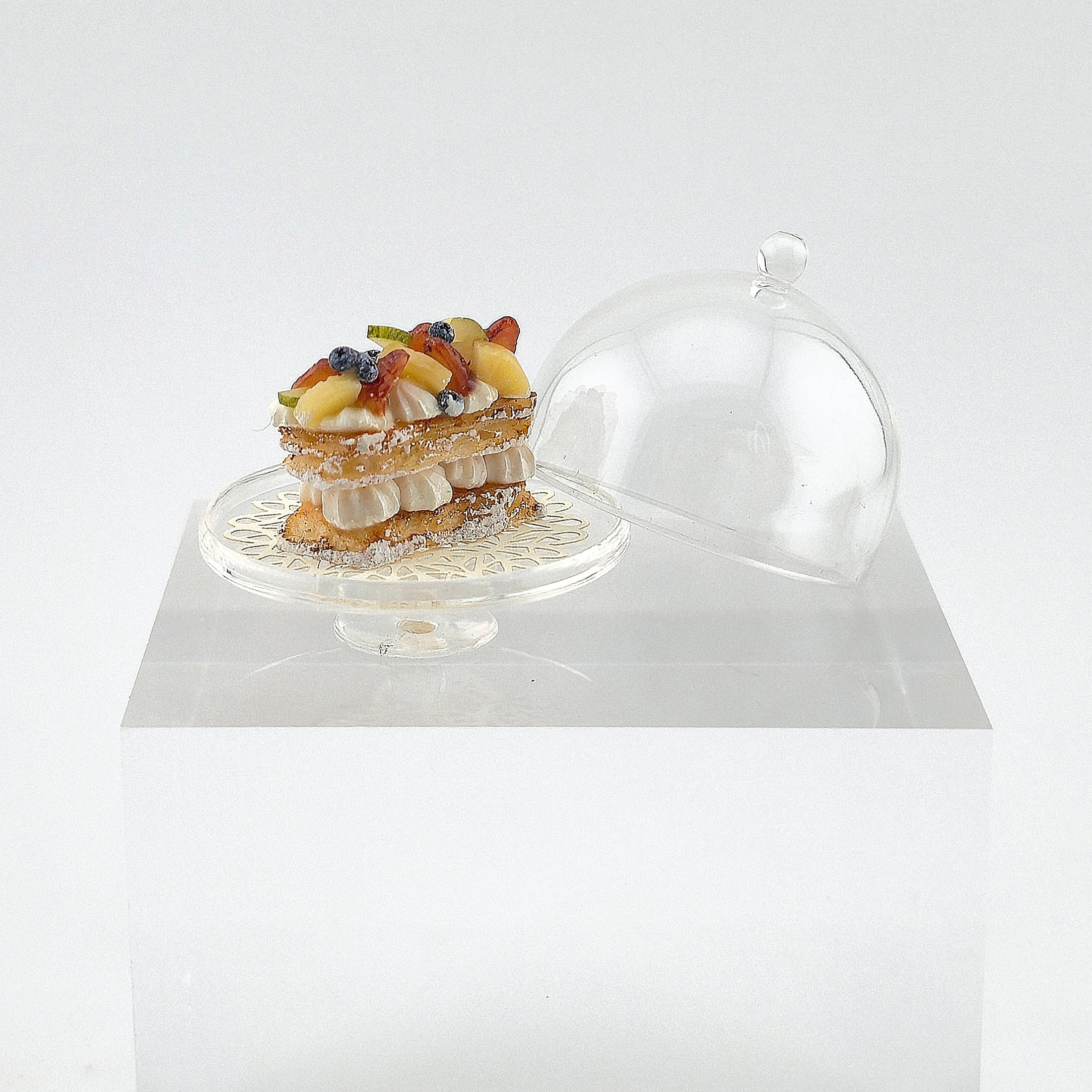 miniature dessert on a cake stand with a transparent dome cover on a white background