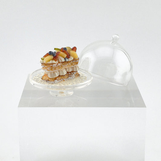 miniature dessert on a cake stand with a transparent dome cover on a white background