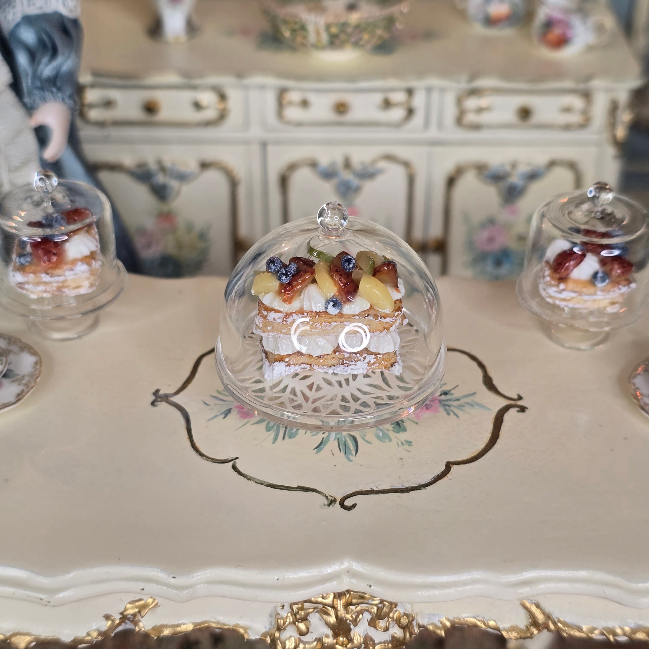 Miniature pastry under a dome on a decorative table with floral patterns