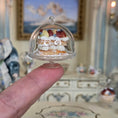 Load image into Gallery viewer, Miniature pastry in a clear dome held by a finger with a decorative background
