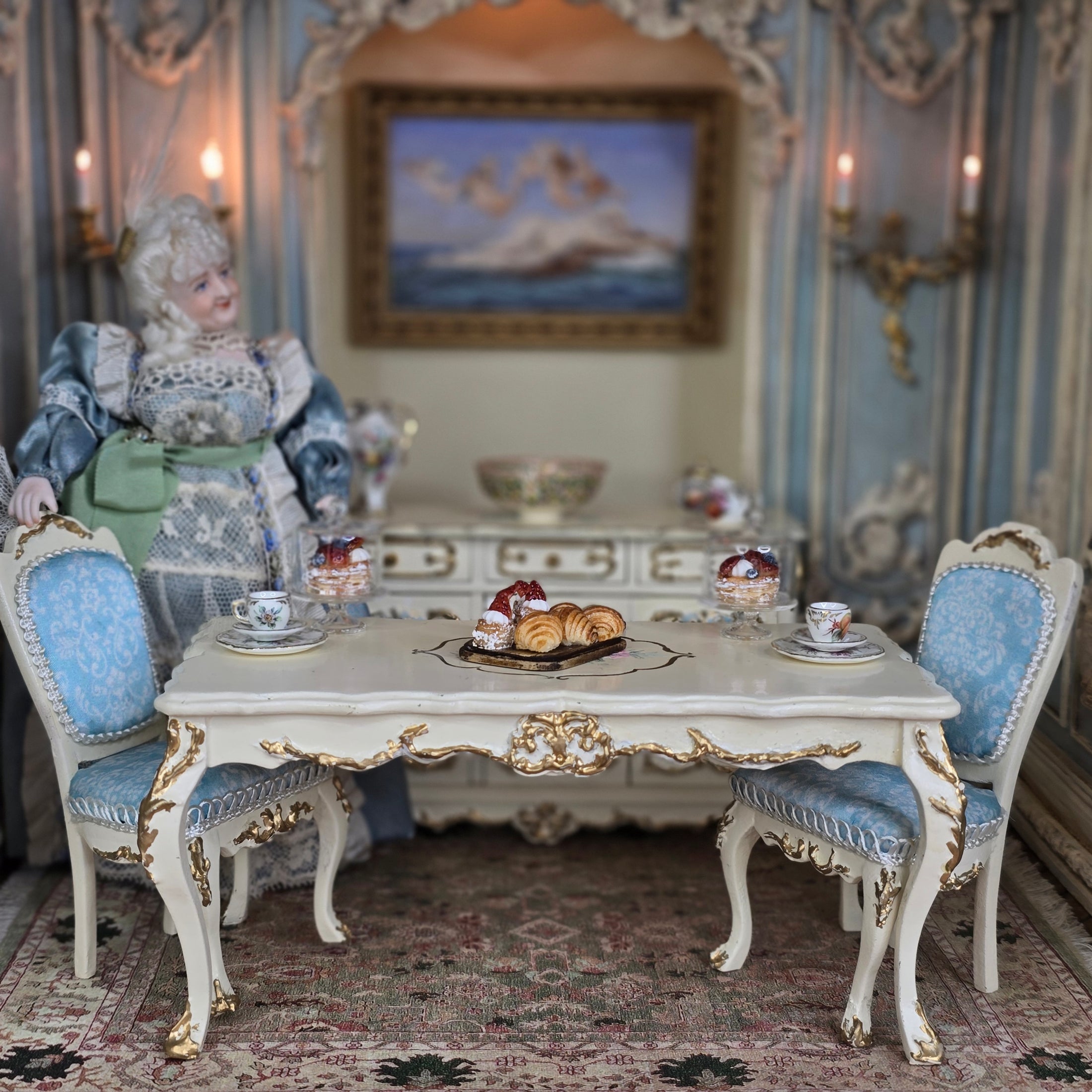 Miniature dollhouse scene with a dining table, chairs, and a doll in an ornate room.
